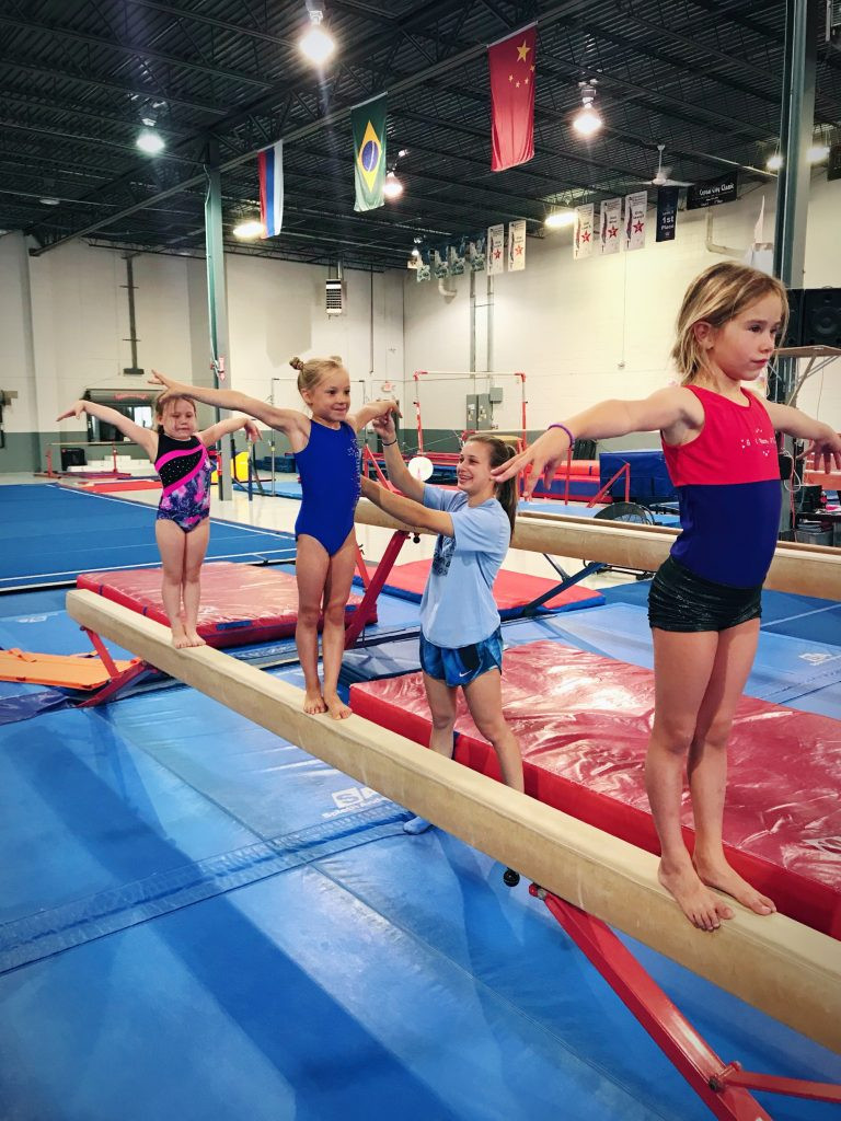 Gymnast performing on balance beam with coach guidance at Euro Stars Gymnastics Plymouth MI