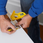 An installer uses a combination square and pencil to mark a measurement where the concealed cabinet hinge would go on the door.