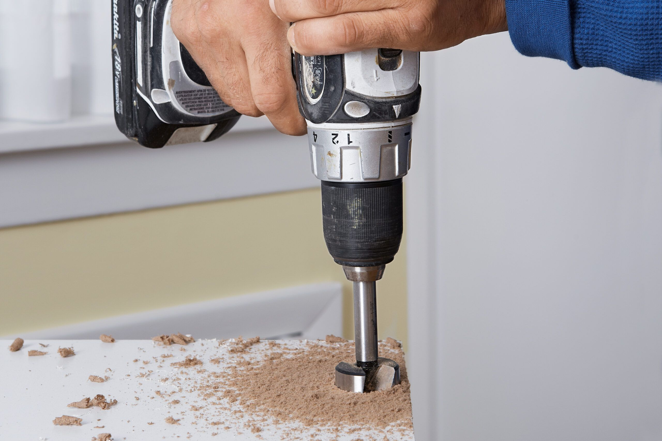 An installer drills the cup holes where the concealed cabinet hinge will go.
