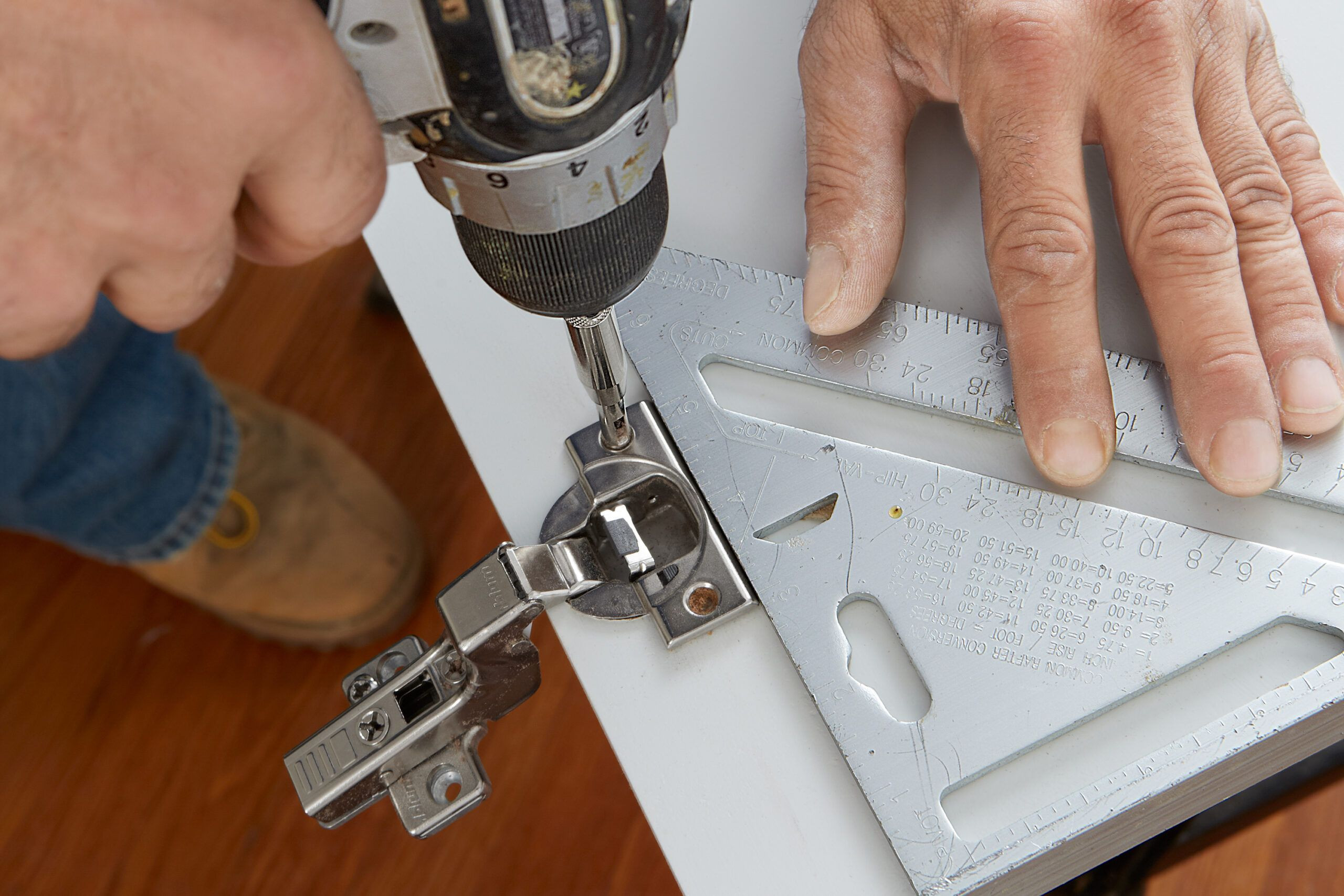 An installer installs the hinge cups into the cabinet using a triangle.